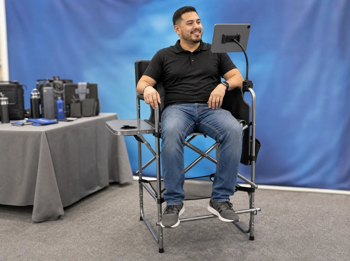 Vendor seated at eye level in a tall director's chair behind a booth table at a trade show
